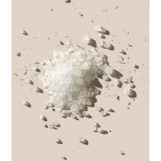 A pile of translucent white bath salts or sugar crystals scattered on a warm beige background.