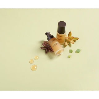 Two Nuva skincare bottles, one with a dark brown pump bottle and one with a dark brown cap, styled with succulent plants and liquid droplets on a pale yellow-green background.