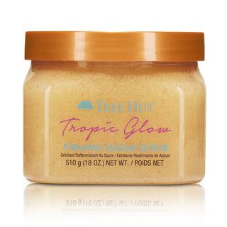 Tree Hut Tropic Glow Firming Sugar Scrub in a clear plastic jar with a metallic bronze lid, shown on a white background with a soft reflection.