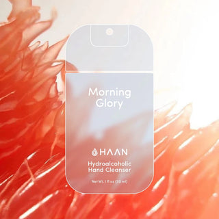 HAAN Morning Glory Hydroalcoholic Hand Cleanser bottle shown against a stylized background of orange-red flower petals with a bright white glow.