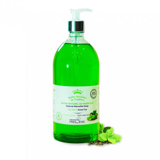 A bottle of Freckins Green Tea Natural Marseille Soap with a green liquid and white pump dispenser, shown on a white background with green tea leaves and herbs at its base.