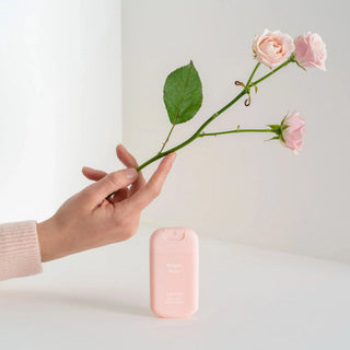 Hand holding a pink rose stem with a pink device on a light background