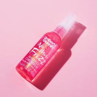 A pink bottle of Umberto Giaminelli No Mote Frizz Anti-Prizz Curl Serum, photographed diagonally on a solid pink background with a strong shadow.