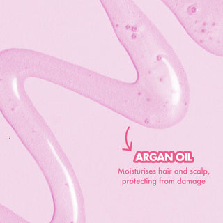 A close-up of a pink cosmetic or hair-care product texture with flowing translucent strands on a pale pink background and text reading 'ARGAN OIL' with a subtitle about moisturising hair and scalp.