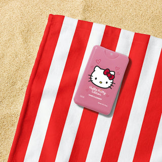 A pink Hello Kitty hand cleaner bottle with a Hello Kitty face graphic, placed on a red and white striped towel on a sandy surface.