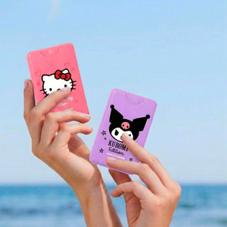 Two hands holding two small Hello Kitty and Kuromi edition card cases, one pink and one purple, against a blurred blue sky and sea background.