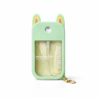 A mint green silicone car keychain spray bottle case with bunny ears, featuring a clear window showing a Pistachio Cake scented hair and body mist inside, complete with a gold keychain ring.