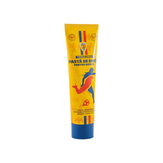 A yellow squeeze tube of dental paste with a blue cap, featuring Romanian text and a graphic of a soccer player, on a plain white background.