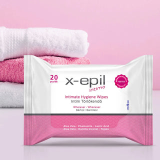 A package of x-epil Intimo Intimate Hygiene Wipes in white packaging with a pink bottom band, shown in front of folded white and pink towels on a soft pink background.