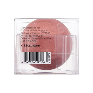 A round makeup sponge in a clear plastic square package, showing the back side with printed text and a barcode. The sponge is a muted dusty rose pink.