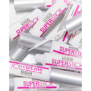 Several tubes of KISS Superstick clear strip lash adhesive are arranged on a white background, with one tube open and its applicator wand placed across the tubes.