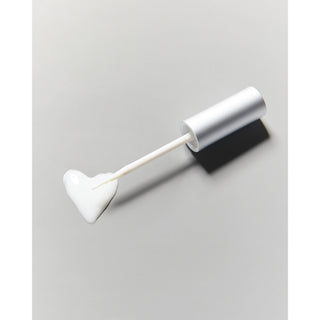 A white cosmetic applicator wand with a heart-shaped doe-foot tip, shown next to its silver cylindrical cap on a light gray background.