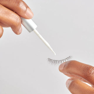 Eyelash extension being applied with a small tool on a neutral background