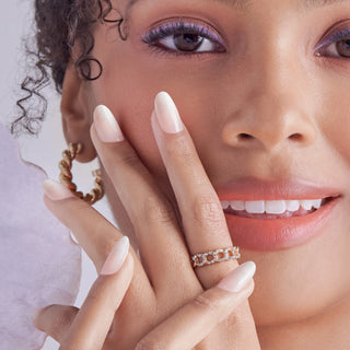 A close-up lifestyle shot of a woman wearing a delicate gold ring with small orange and white stones on her ring finger, with her hand resting against her cheek.