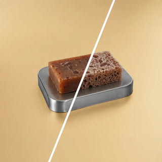 Bar of soap and sponge on a metal soap dish against a beige background