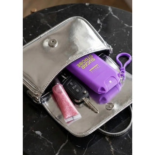A silver metallic handbag shown open on a black marble surface, with a purple car key case labeled 'SUGAR STORAGE' and other small items inside.