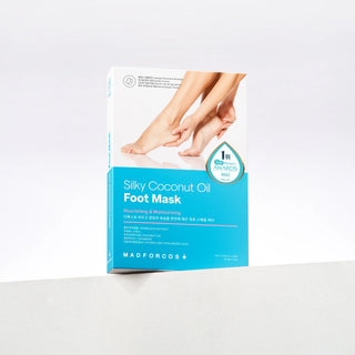 A boxed foot mask product standing upright on a white surface against a white background. The package is mostly white with a bright blue lower section and shows a photo of bare feet on the front.