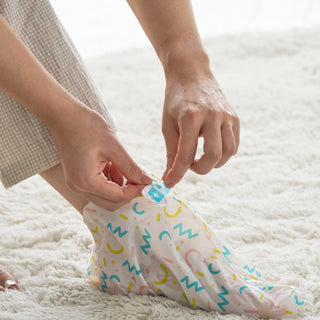 A person's hands fastening a clear plastic foot bag with a colorful confetti print, placed on a white shag rug.