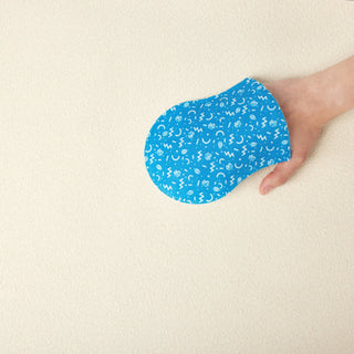 A hand holding a blue, oval-shaped silicone or fabric patch with a white pattern, set against a plain, textured beige background.