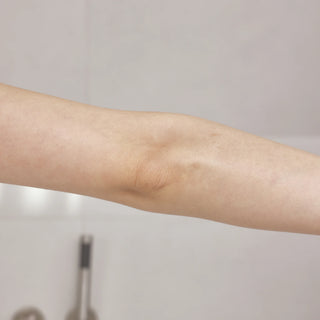 A close-up of a human forearm and elbow against a soft, light gray background.
