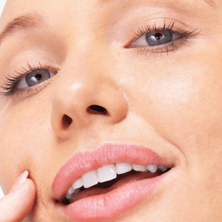 Close-up of a woman's face showing clear, smooth skin and healthy white teeth, with her hand touching her cheek.