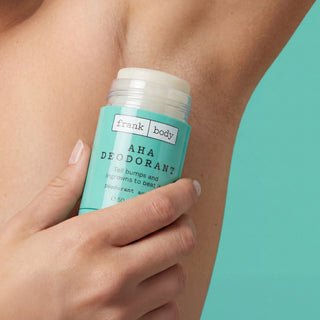 A close-up of a hand holding a teal Frank Body AHA Deodorant stick against a person's armpit, with a solid teal background.