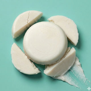 A round white solid bar product, likely soap or shampoo, centered on a mint green background with several cut wedges and a smear around it.