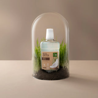 Sticla de apa de gura Ecodenta sub un glob de sticla, pe iarba, cu fundal bej