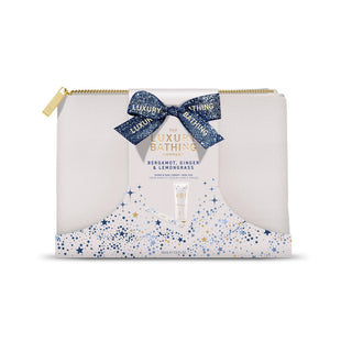 The Luxury Bathing Club Bergamot, Ginger & Lemongrass gift set in a white zip pouch with a blue glitter ribbon bow, gold zipper, and blue/gold star-patterned lower section.