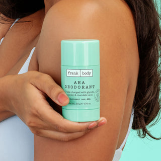 A person holding a mint green Frank Body AHA Deodorant stick against their upper arm, with the product label clearly visible.