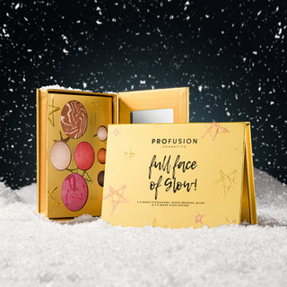 Profusion Cosmetics 'Full Face of Glow!' holiday gift set displayed in a snowy scene. The set includes a gold makeup palette with colorful pressed powders and a matching gold folding card in the foreground.