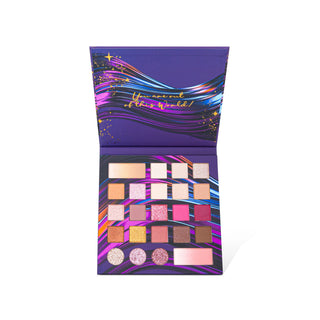 An open eyeshadow palette with a purple cover and interior featuring multicolored abstract streaks and gold script text. The palette contains multiple square and circular pans in shades of pink, purple, gold, brown, and beige, arranged in a grid on a white background.