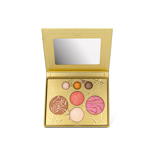 An open gold makeup palette with a mirror in the lid and six round eyeshadow pans in pink, peach, brown, and light pink shades, set against a plain white background.