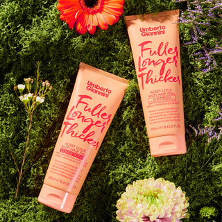 Two bottles of Umberto Giannini 'Fuller Longer Thicker' hair product on a green background with flowers.
