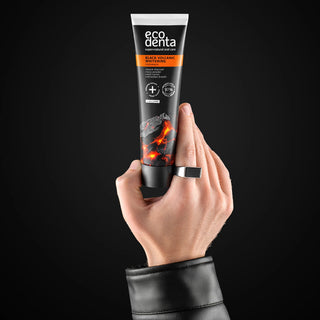 Mana tinand un tub de pasta de dinti Ecodenta Black Volcanic Charcoal, pe fundal negru