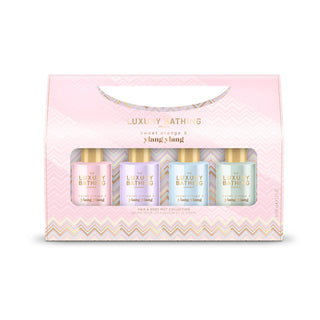 A pink gift box set for luxury bath products, featuring a clear window that displays four small bottles in pastel pink, lavender, light blue, and mint green, with gold lettering. The box has a chevron pattern at the bottom and a curved cutout handle at the top.