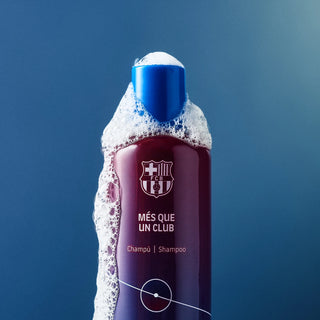 Sticla de sampon mov cu logo FC Barcelona si capac albastru, pe fundal albastru