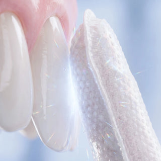 A close-up of a translucent, textured dental curing light or gel applicator touching white teeth, with soft pink gums and a bright, sparkling blue-white background.